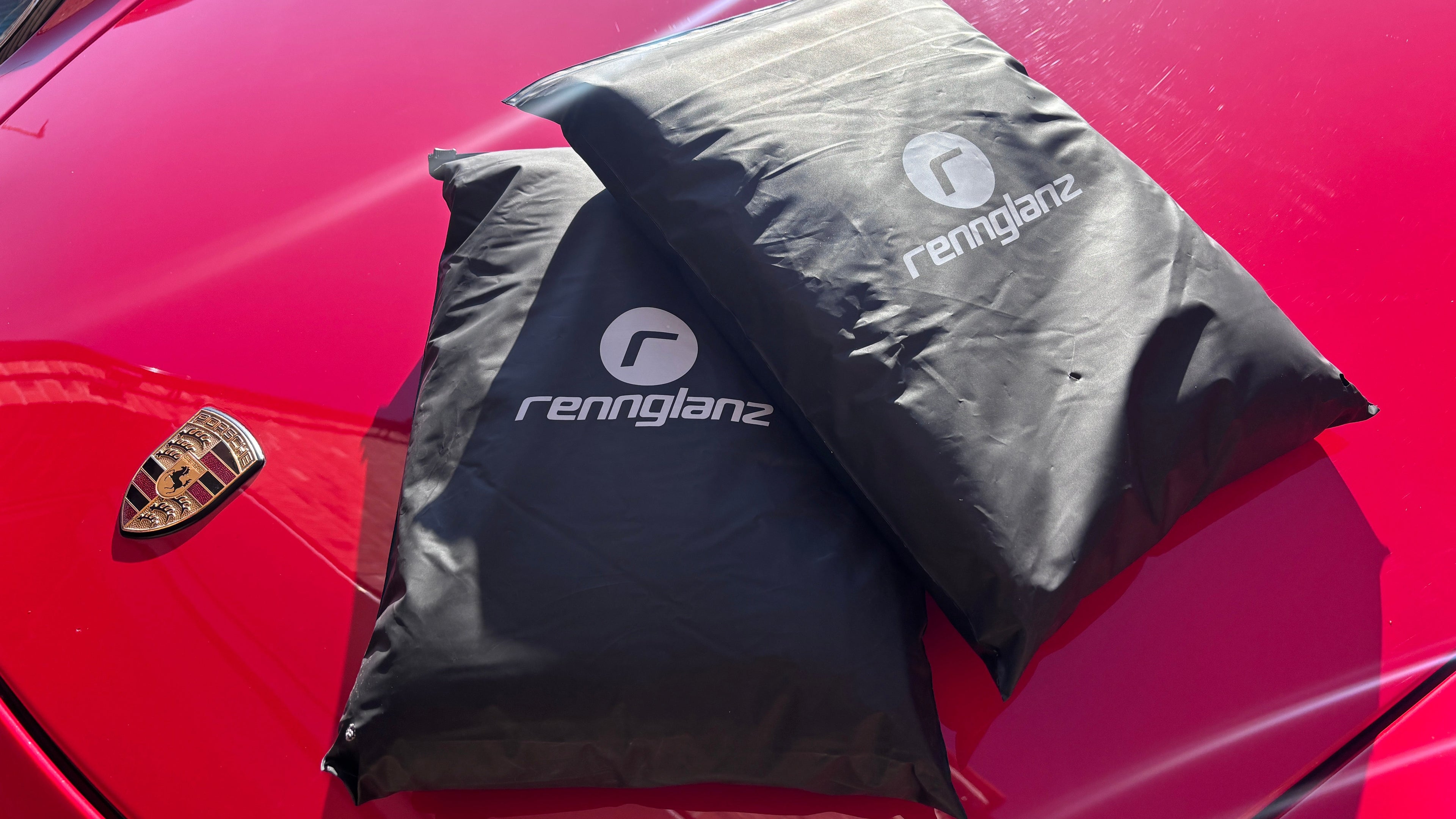 Two black car covers with 'rennglanz' branding on a red car.